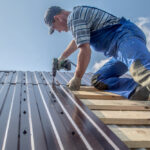 Male,Builder,Performs,Work,On,The,Roof,,Fastens,Corrugated,Sheets